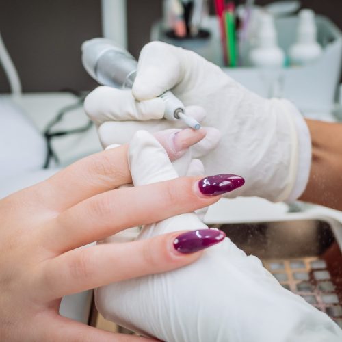 A professional esthetician using an electric nail file drill to remove acrylic gel from nails